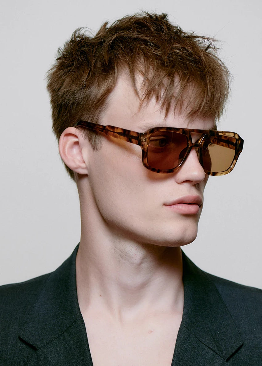 Man wearing tortoiseshell sunglasses with a neutral background