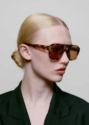 Person wearing a stylish outfit with sunglasses against a plain background