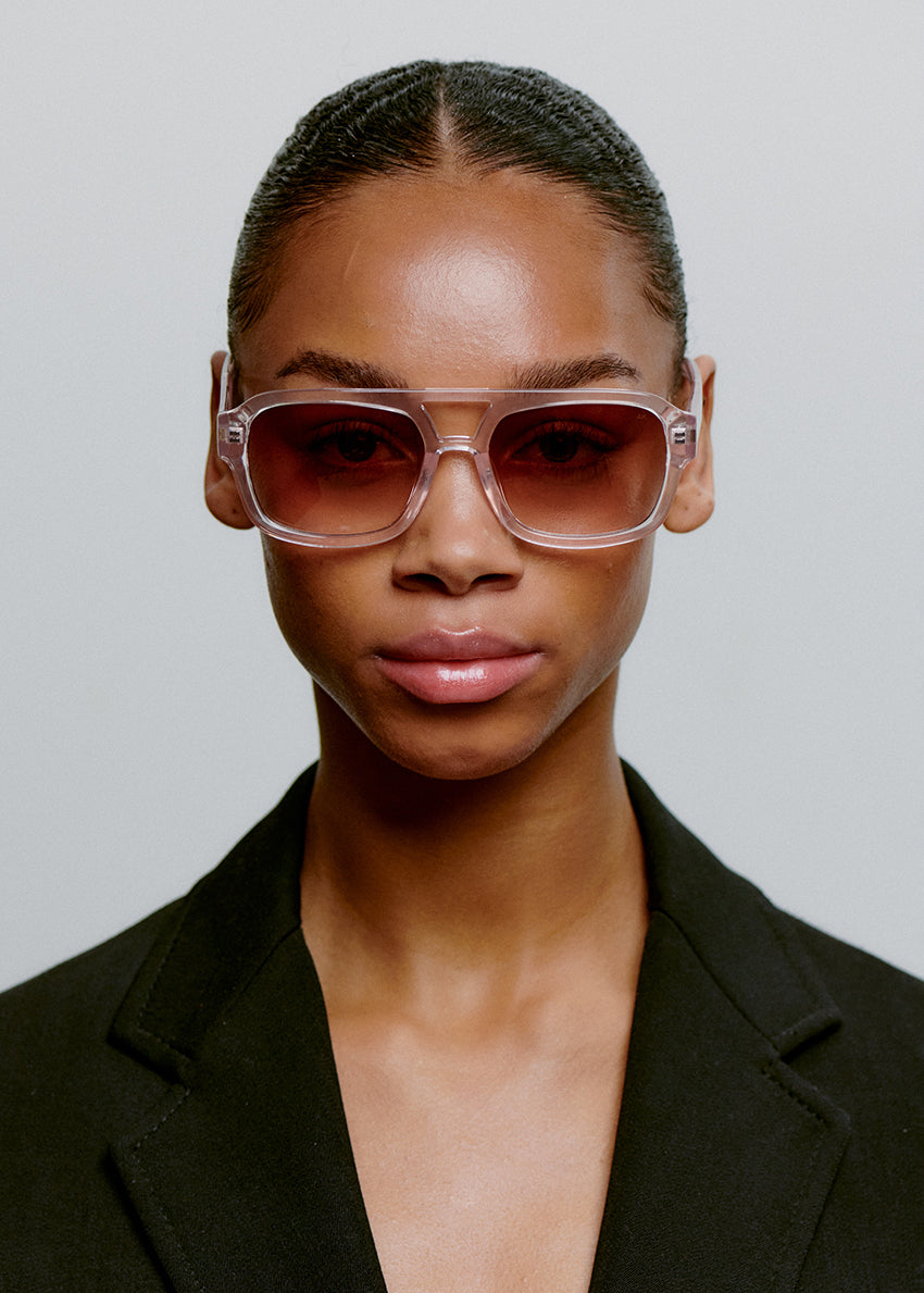 Person wearing large sunglasses and a black blazer against a neutral background
