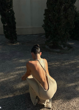 Person wearing a beige dress sitting on the ground with trees in the background