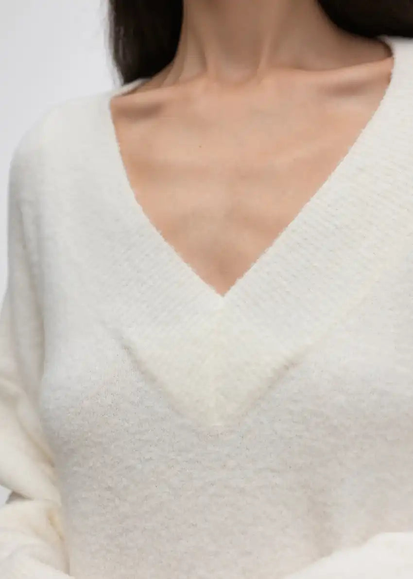 Wide knitted white top, with a V rib neckline and ribbed cuffs, made of fluffy blended wool yarn.