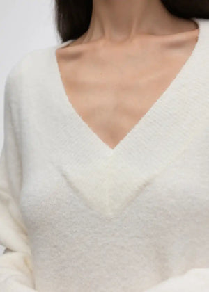 Wide knitted white top, with a V rib neckline and ribbed cuffs, made of fluffy blended wool yarn.