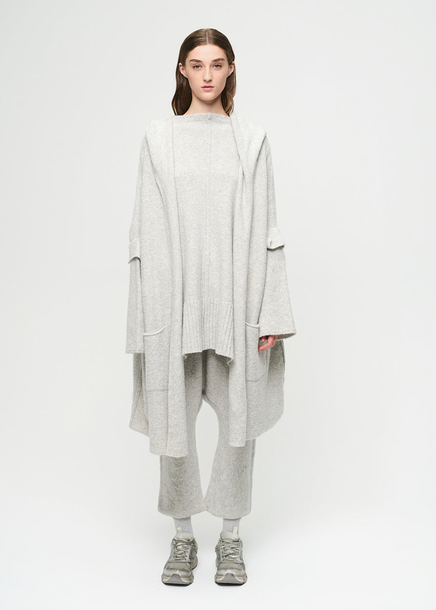Person wearing a long light gray cardigan over a gray sweater and pants on a white background