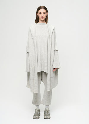 Person wearing a long light gray cardigan over a gray sweater and pants on a white background