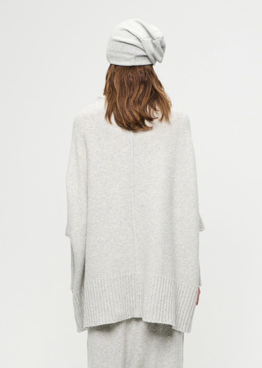 Person wearing a light gray sweater and beanie on a white background