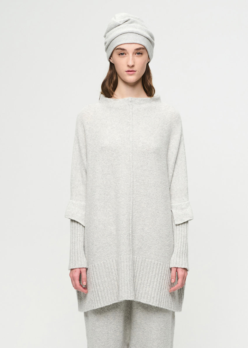Person wearing a light gray sweater and pants with a white beanie on a white background
