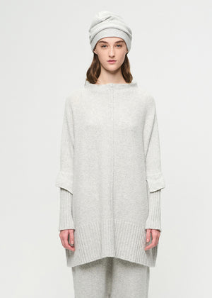 Person wearing a light gray sweater and pants with a white beanie on a white background