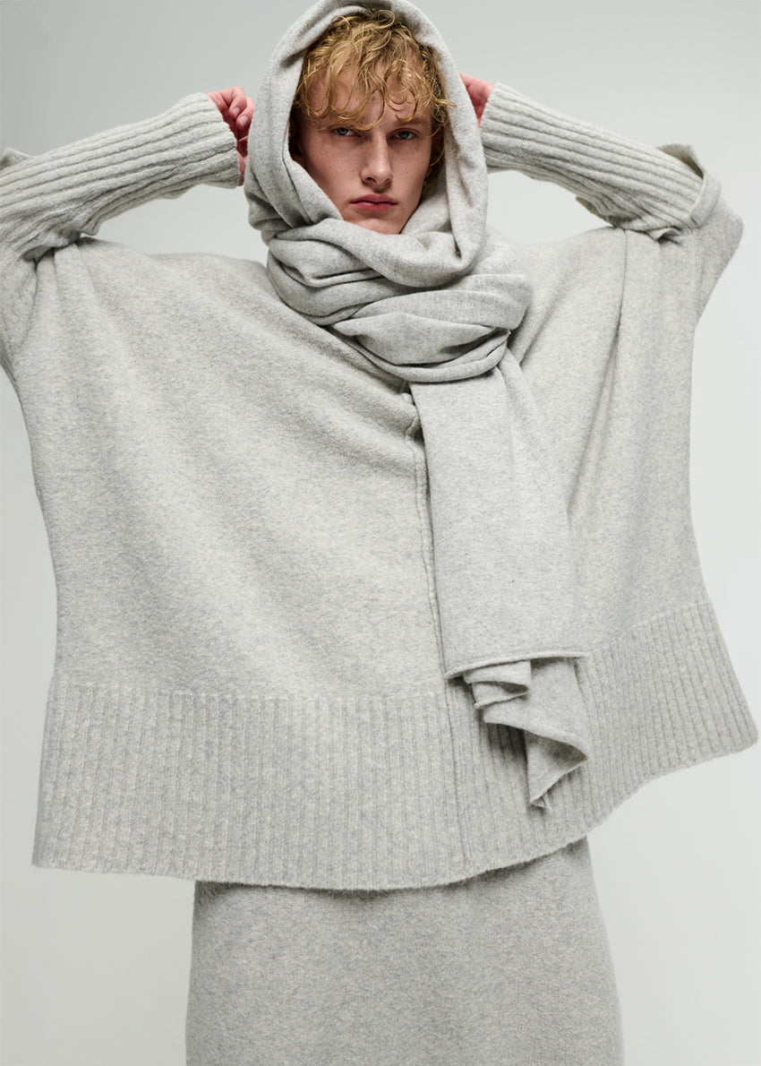 Person wearing a gray sweater and scarf against a plain background
