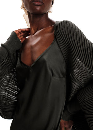 Person wearing a dark green dress with a textured gray cardigan on a white background