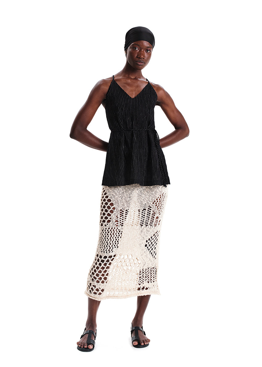 Woman wearing a black sleeveless top and white patterned skirt on a white background