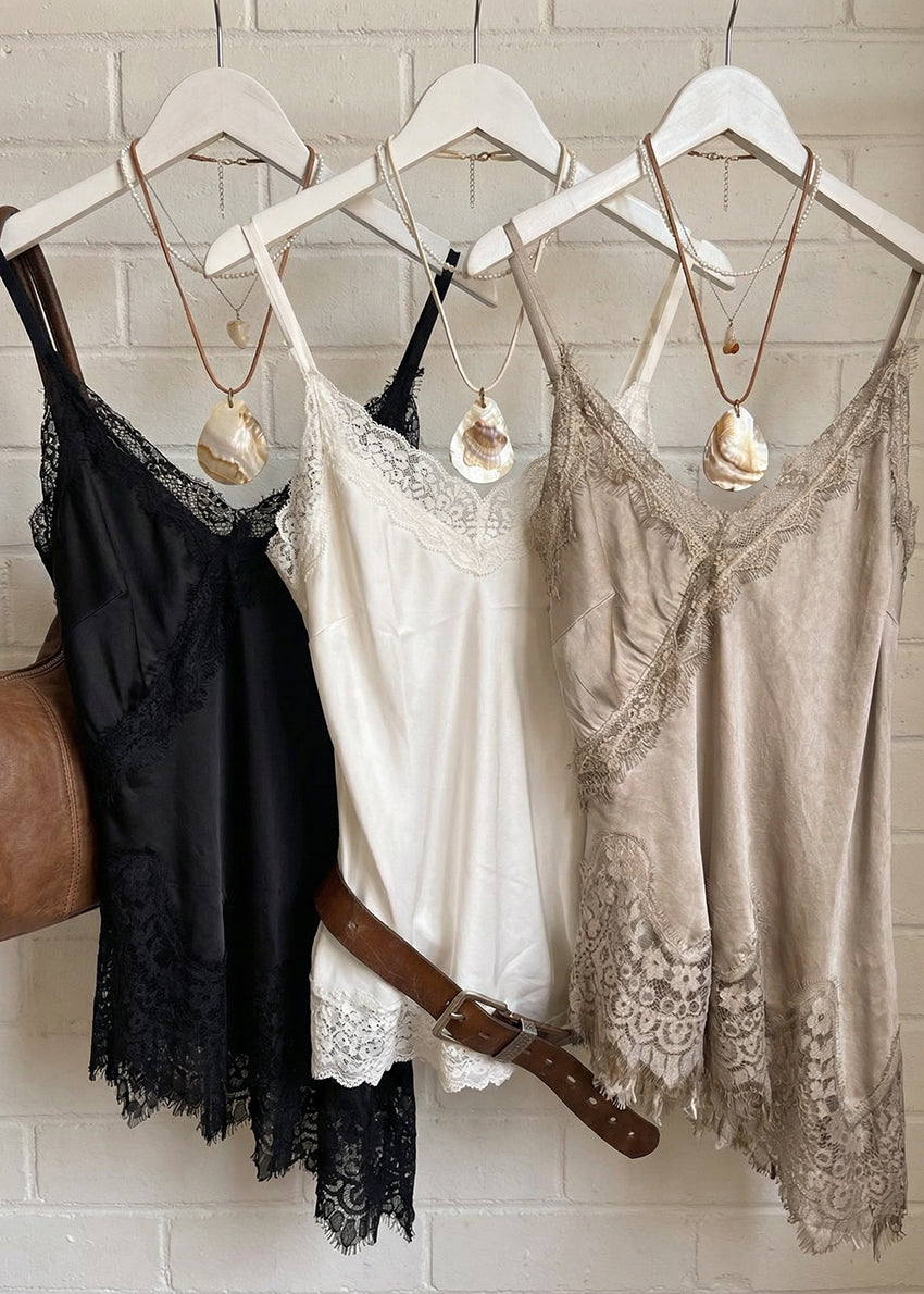 Three lace-trimmed camisoles hanging on a rack against a tiled wall.