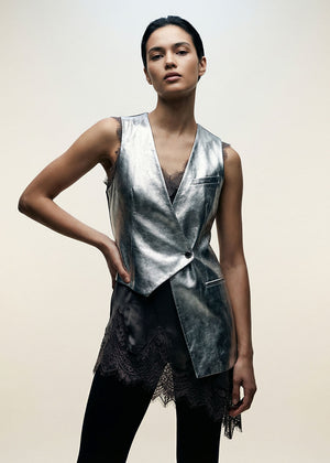 Woman wearing a metallic silver vest over a black top with a beige background