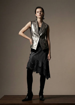Woman wearing a metallic vest and black dress against a plain background