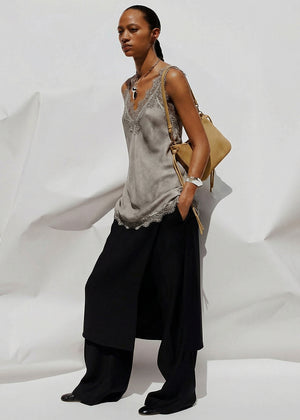 Woman wearing a gray lace top and black pants against a white background