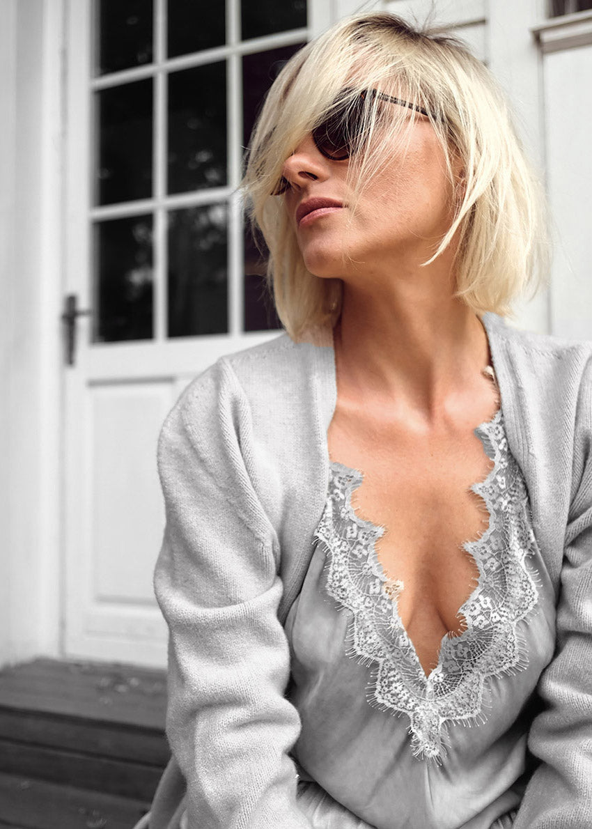 Woman wearing a light gray cardigan with lace detailing in front of a white door.