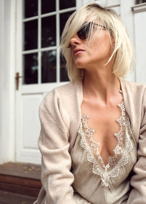 A person wearing a wheat sleeveless top with lace trim, accessorized with a cardigan and sunglasses.