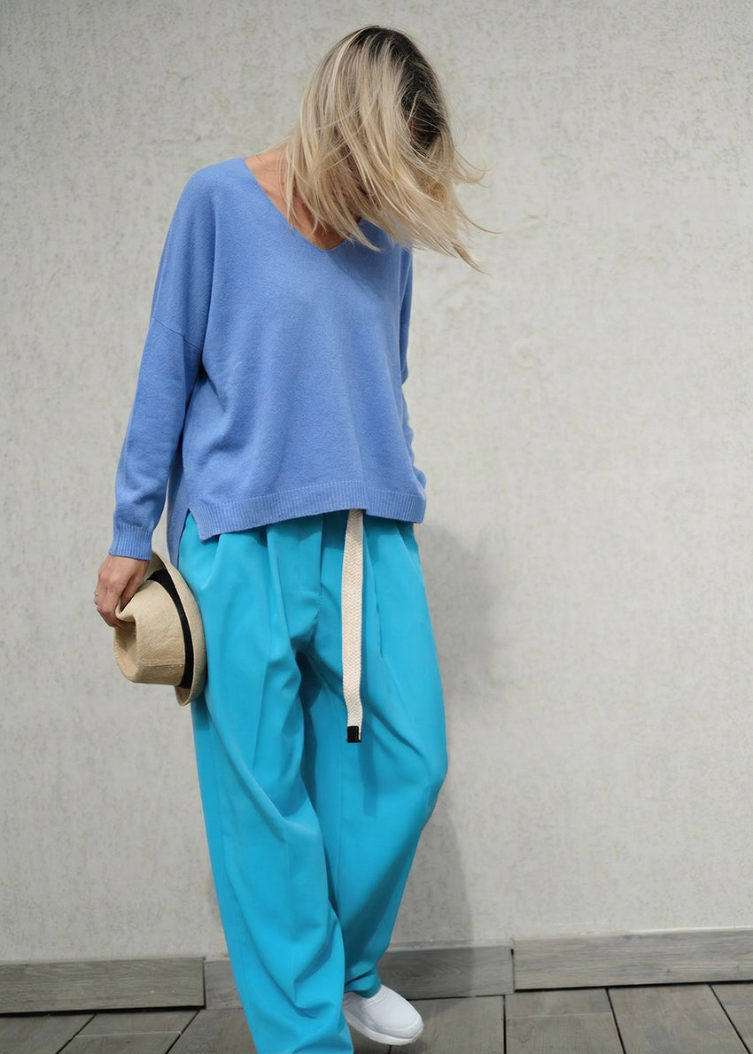 Person wearing a blue sweater and light blue pants holding a hat against a plain background