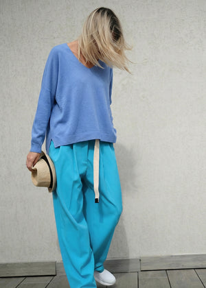 Person wearing a blue sweater and light blue pants holding a hat against a plain background