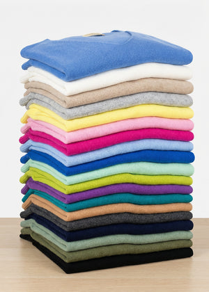 Stack of folded colorful sweaters on a wooden surface with a white background