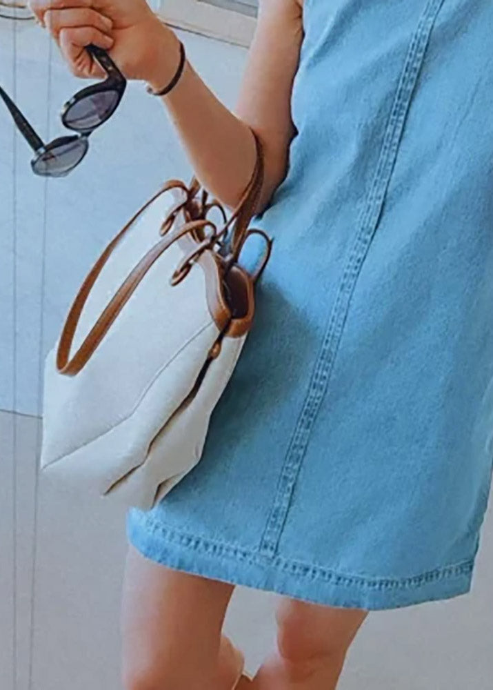 Person holding a white handbag with brown leather strap and sunglasses, wearing a blue dress.