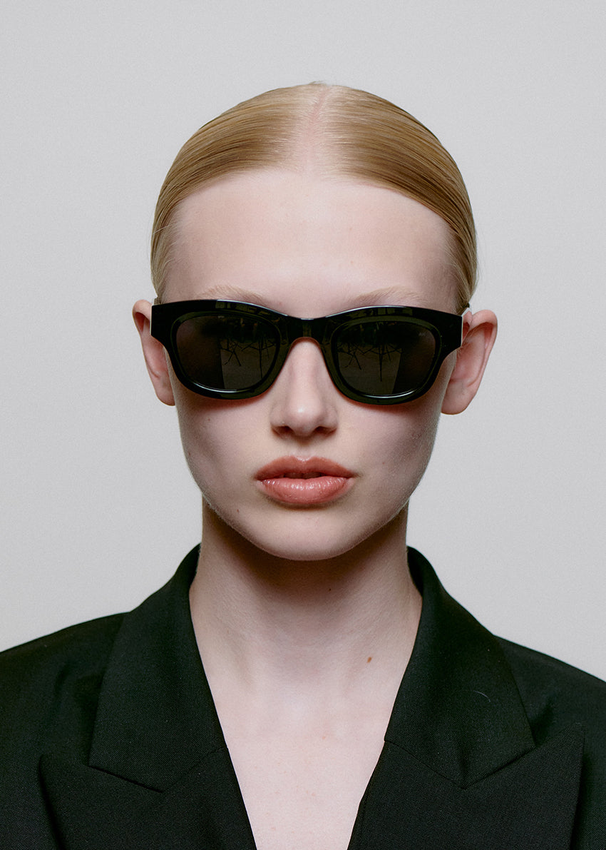 Person wearing black sunglasses and a black outfit against a plain background