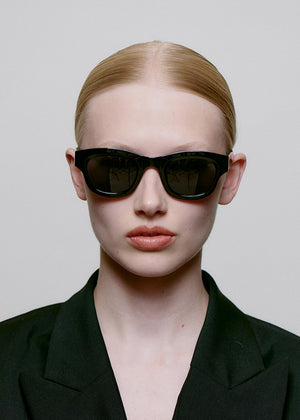 Person wearing black sunglasses and a black outfit against a plain background