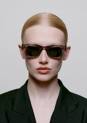 Model wearing dark sunglasses and a black outfit against a plain background