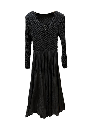 A black crepe dress with a fitted top and voluminous skirt, featuring straight and pleated long sleeves, photographed against a white background.