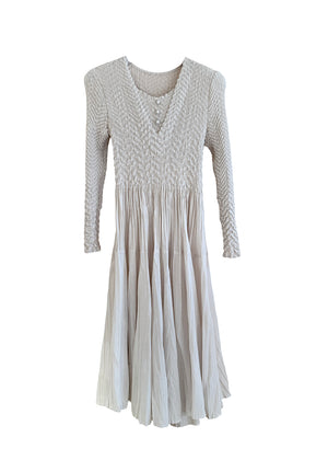 A beige crepe dress with a fitted top and voluminous skirt, featuring straight and pleated long sleeves, photographed against a white background.