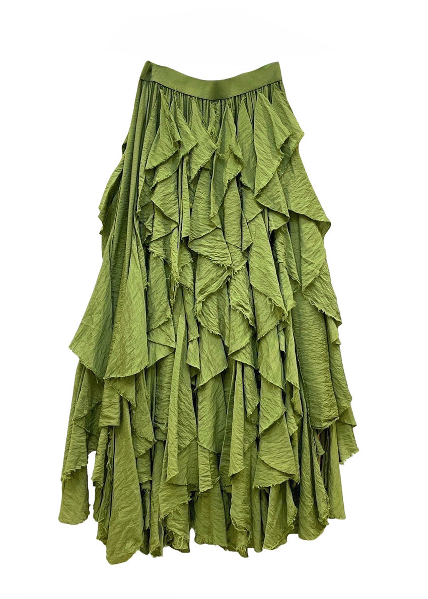 Woman in a green ruffled skirt and white top standing on a beach.