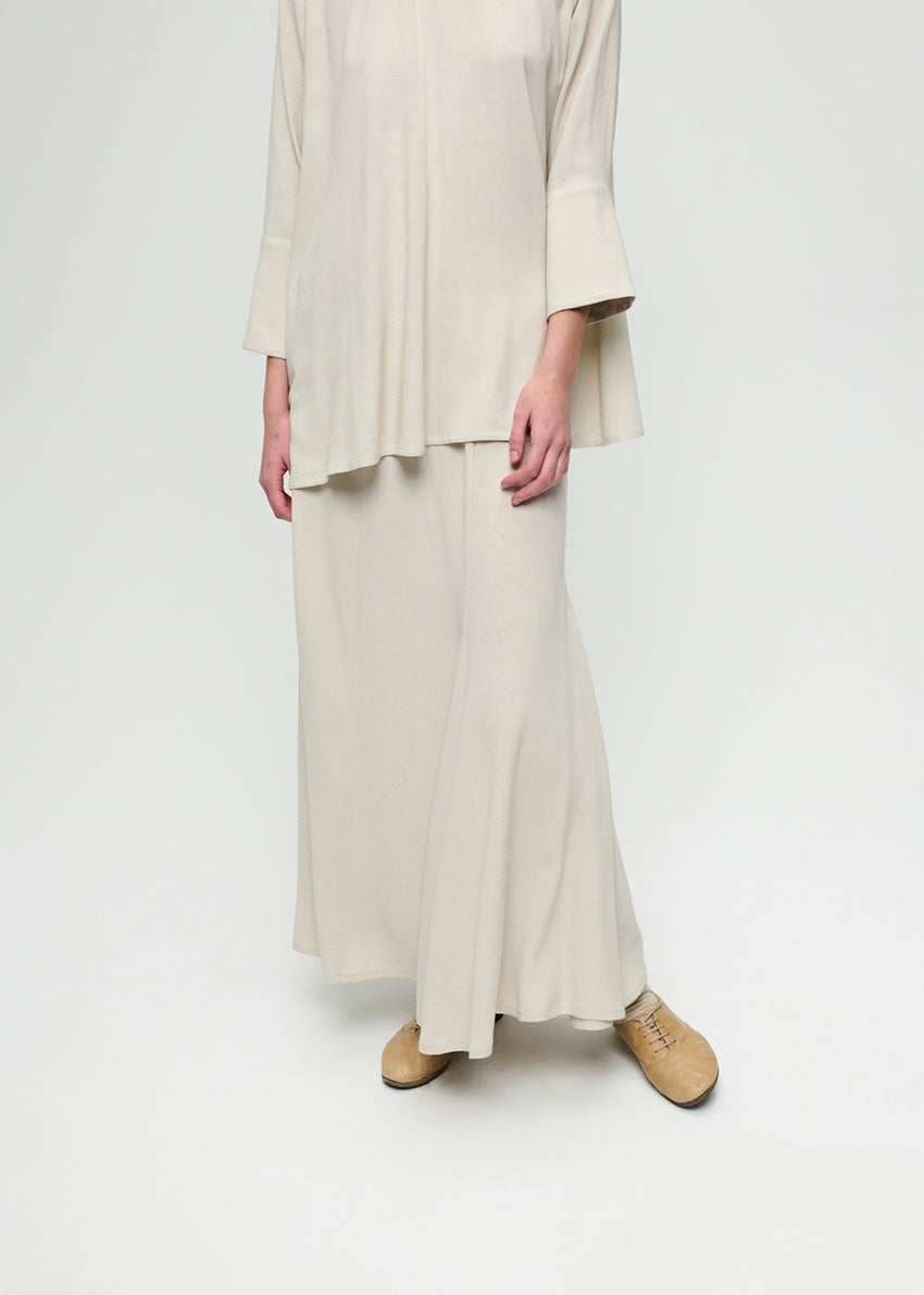 Person wearing a beige outfit with a long skirt and jacket on a white background