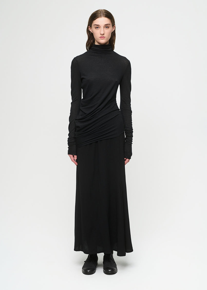 Woman wearing a black top with a draped effect and a black skirt on a white background