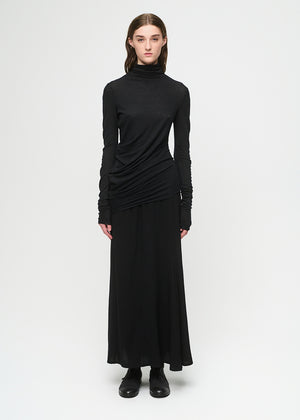 Woman wearing a black top with a draped effect and a black skirt on a white background