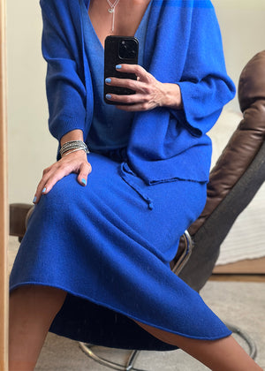 A person seated wearing a blue skirt and matching top, holding a smartphone in their hand.