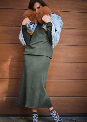 A person wearing a jeans jacket with dark olive green sweater and skirt 