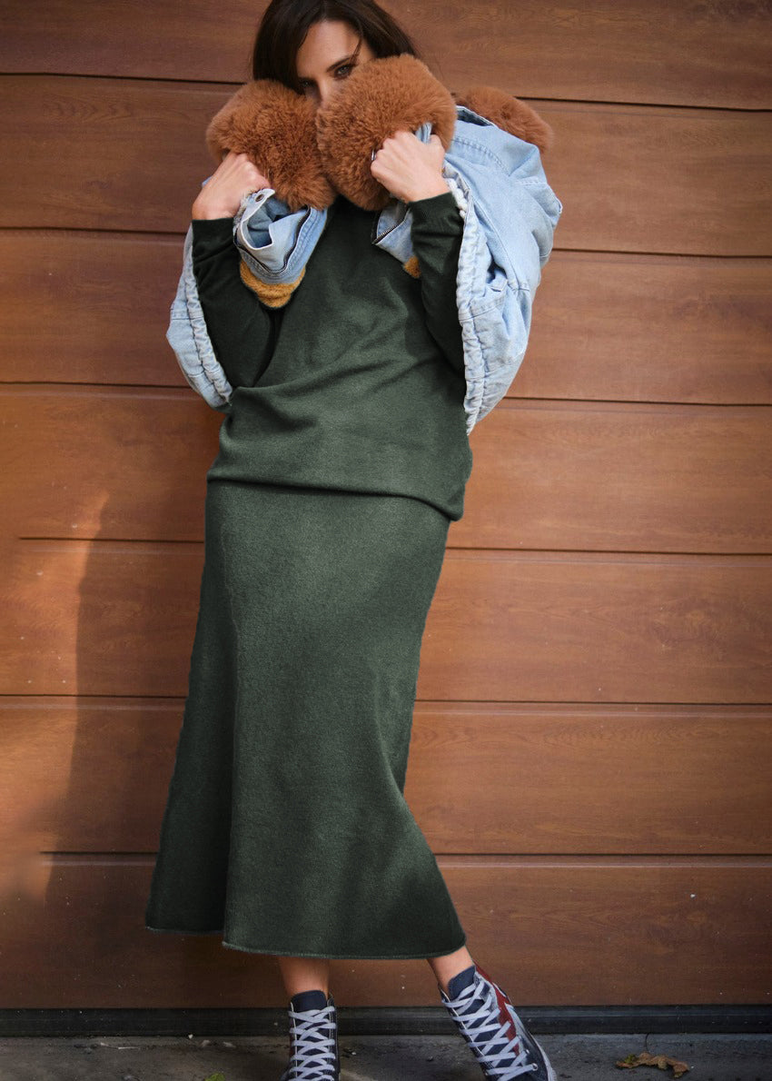 A person wearing a jeans jacket with a matching set of dark olive green sweater and skirt
