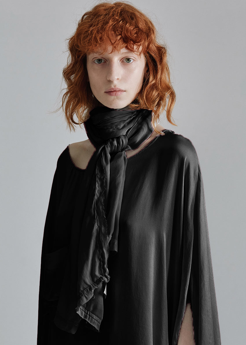 A person wearing a black satin silk scarf with frayed edges, tied around the neck.