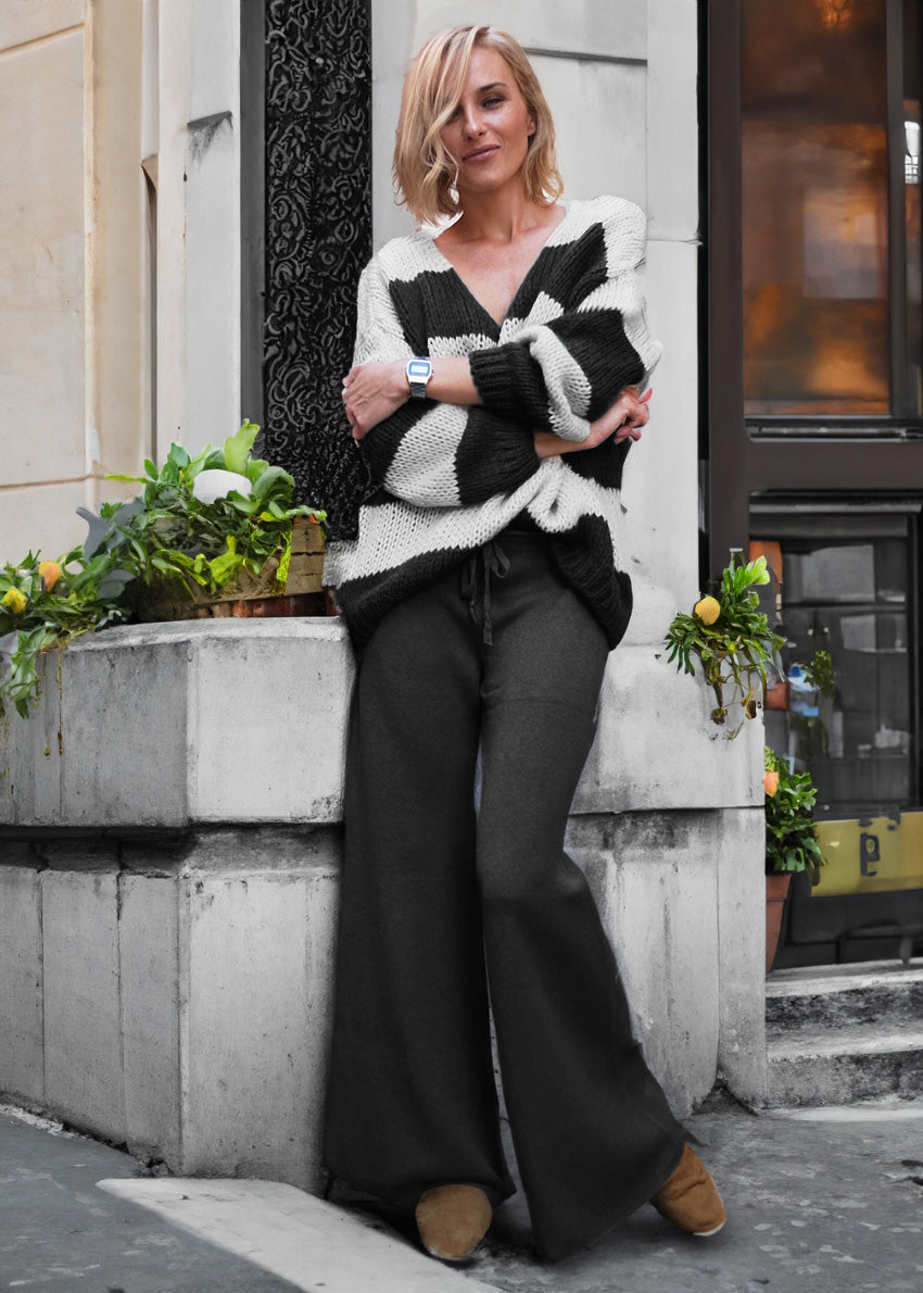 A person wearing a black and white striped sweater with long sleeves, paired with wide-leg black pants, standing on a city street.