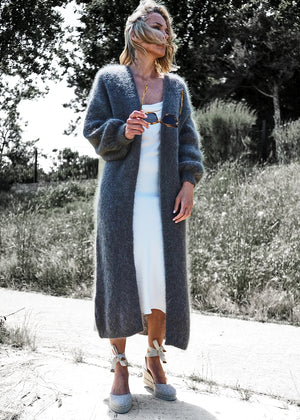 Person wearing a dim grey mohair long cardigan with a white dress on a forest road