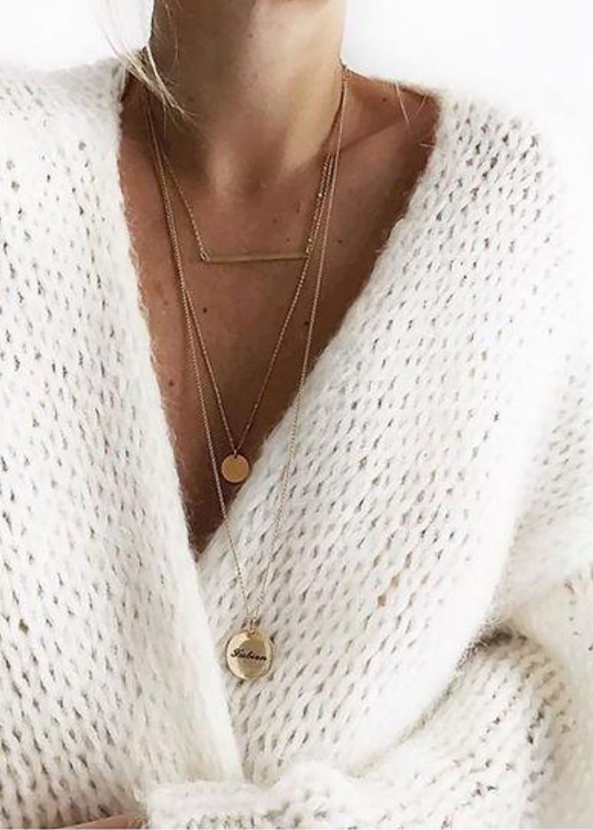 Close-up of a person wearing a white knit cardigan with layered gold necklaces.