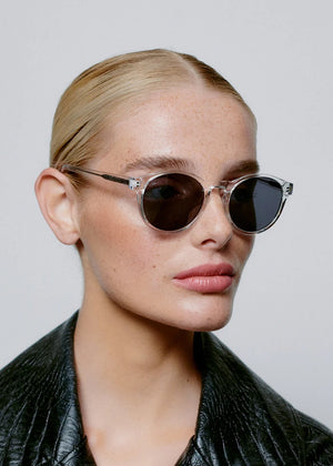 Person wearing round sunglasses and a black leather jacket against a plain background