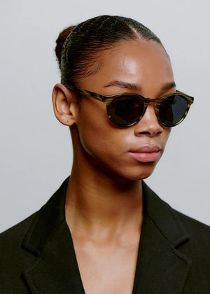 Woman wearing sunglasses and a black blazer against a neutral background