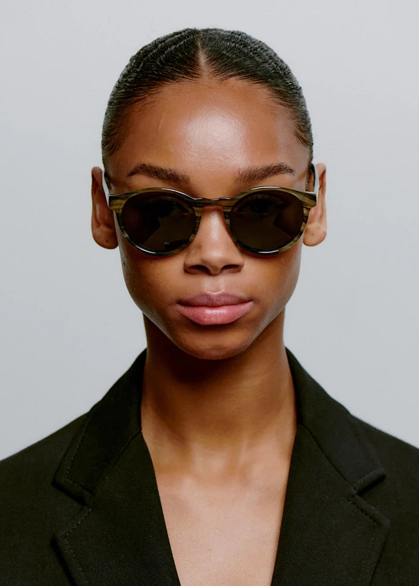 Person wearing dark sunglasses and a black blazer against a plain background