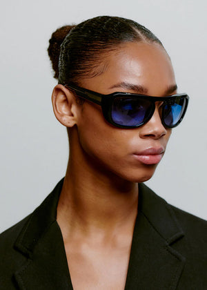 Person wearing black sunglasses and a black jacket against a plain background