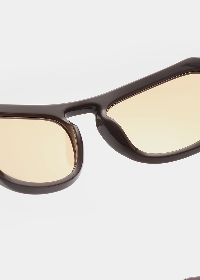 Sunglasses with brown frame and yellow-tinted lenses on a light gray background