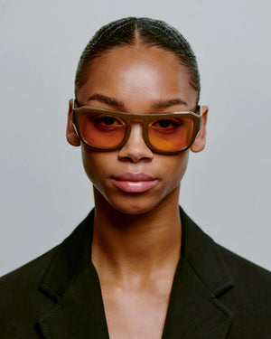 Person wearing a stylish outfit with sunglasses against a plain background