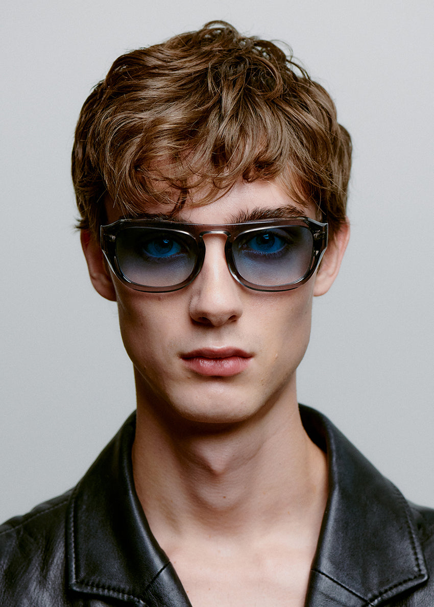 Man wearing sunglasses and a black leather jacket against a gray background