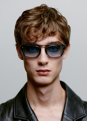 Man wearing sunglasses and a black leather jacket against a gray background