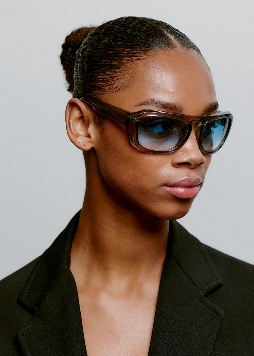 Woman wearing sunglasses and a black blazer against a neutral background