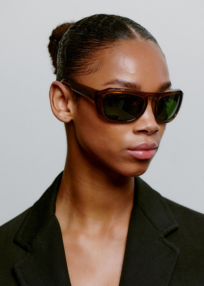 Woman wearing sunglasses and a black blazer against a neutral background